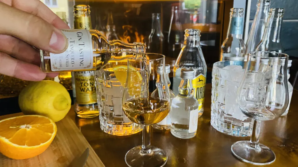 Gin wird aus einer Probierflasche in ein Nosingglas gegossen, daneben Tonic und Zitrusfrüchte